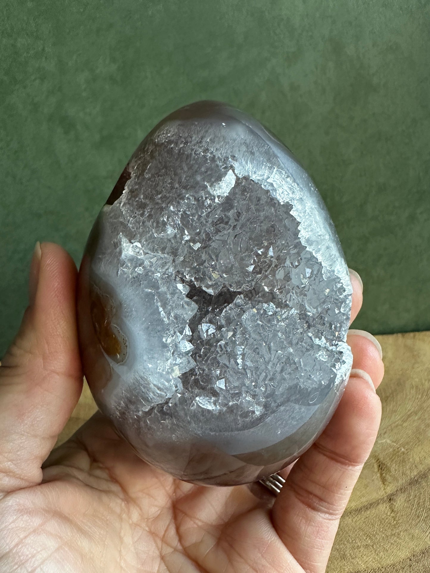 Hand holding a rough-textured rock against a green and wooden background